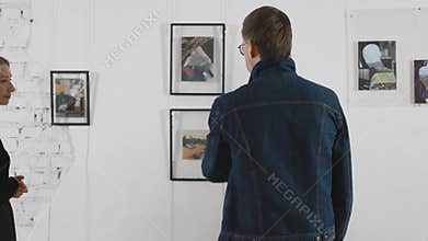 In an art gallery, at an exhibition of abstract paintings. A man and a woman are discussing objects of contemporary art