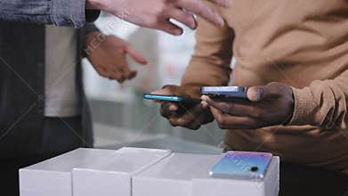 A consultant in an electronics store offers a choice of new smartphones to an African man.