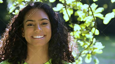 African American girl biracial teenager young woman outside smiling, laughing and turning to camera standing under a tree