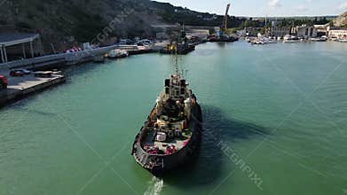 A cinematic flight behind a tugboat. The ship returns to the parking lot after work. Technical port. The sea is greenish in color.