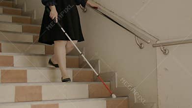 Woman with blindness disability walking down stairs using blind walking stick or long cane and touching stair handrail