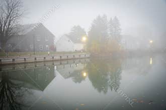 Foggy morning scenic Erie canal with reflection of historic two-story houses, pole lighting and colorful fall foliage riverside