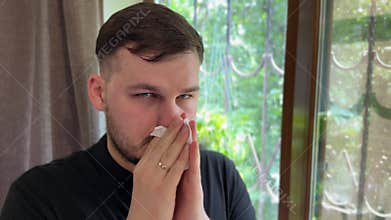 Man with teary eyes wipes nose, clearly affected by allergies