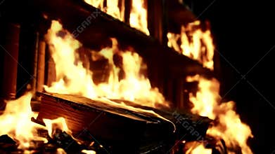 Close-up shot of antique books on a wooden bookshelf engulfed by intense flames in the dark