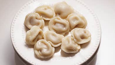 Boiled dumplings with dill are arranged in a circle on a white plate.