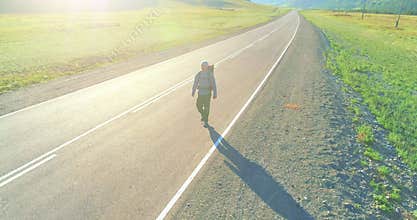 Flight over hitchhiker tourist walking on asphalt road. Huge rural valley at summer day. Backpack hiking guy.