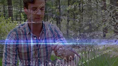 Man entering clearing, crouching inspecting tall grass, tapping watch, technology overlays scanning