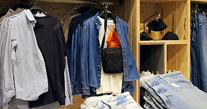 Various shirts, denim jackets, jeans, and accessories are neatly displayed on hangers and shelves in a modern clothing