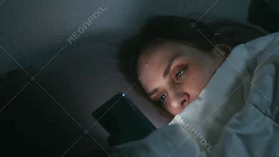 Woman browsing smartphone in bed at night