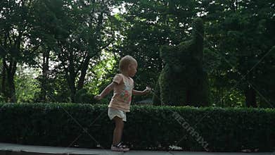 Little child playing with hedge in city park, having fun