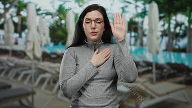 Woman making oath gesture by swimming pool setting with a serious expression, conveying sincerity and commitment in a peaceful