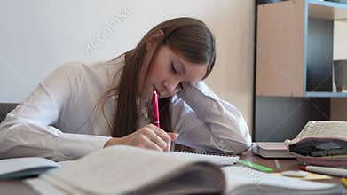 girl is doing homework. A girl in a white blouse gets bored while doing homework. A female student is tired in class. A schoolgirl