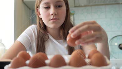 Caucasian girl chooses eggs from a cardboard box to cook fried eggs in the kitchen.