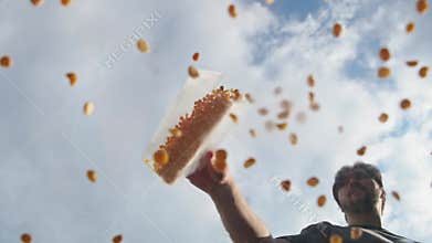 Man gradually empties substantial quantity of dried ground peas or chickpeas from container onto clear glass in open air. Low