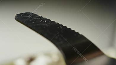 Extreme Close-Up: Serrated Knife Spreading Creamy Green Substance