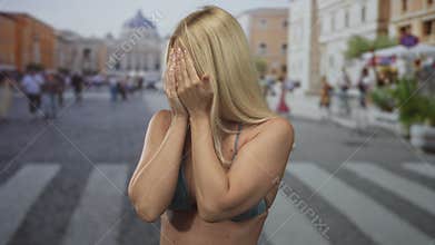 Woman covers face with both hands in busy st peter square outside vatican basilica san pedro while wearing bikini top;
