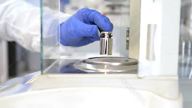 A operator's hand is holding steel calibration weight to place on the analytical balance.