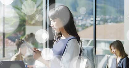 Office woman glancing at smartphone, lifting phone and scrolling data by window with bokeh overlays