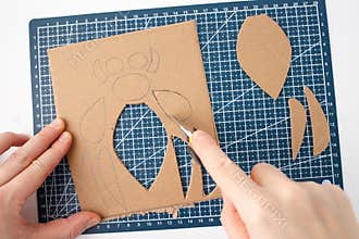 top down view of hands cutting cardboard with utility knife on cutting mat with a grid design, flat lay style,
