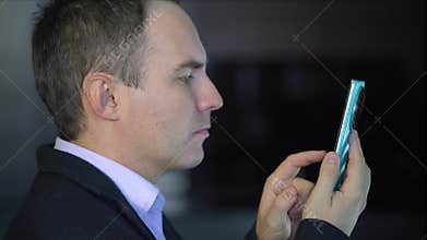 A young man is carefully reading messages on a smartphone. thoughtful businessman in pink t-shirt holding a phone and