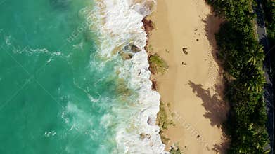 Erial of foamy sea waves meeting the soft sand on the beach with a road surrounded by greenery ne