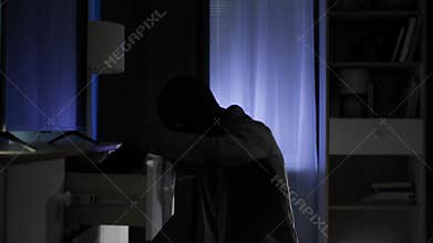 home security, male thief wearing balaclava and rummaging through things looking for valuable things and money in the