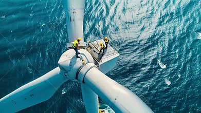 People works on top of wind turbine in sea, engineers perform maintenance of windmill in ocean, aerial view