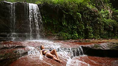 girl with bikini lying down in waterfall river