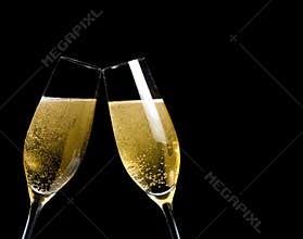Two champagne flutes with golden bubbles make cheers on black background