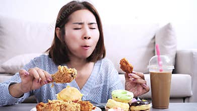 asian woman happily eating fast food like fried chicken, with donuts, cake, burgers, and sweet coffee on the table