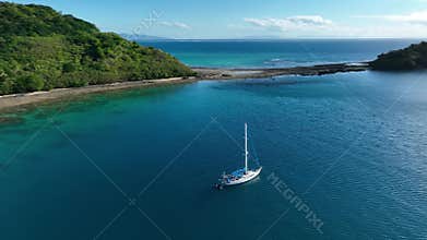 Aerial top down view, a anchored sailboat off the coast of an island.