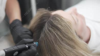 Close-up of HydraFacial Keravive scalp treatment on a woman with thick blonde hair. The aesthetician uses the original