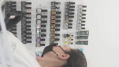 Nail technician in black gloves selecting a gel polish bottle from an organized wall display. Ideal for beauty salon