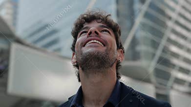 Portrait of happy Hispanic businessman smiles and observes skyscrapers in city