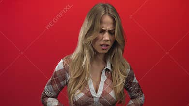 Woman holding abdomen in red studio with furrowed brow tense posture and pained expression; stomachache discomfort