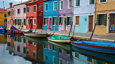 Colorful boats float gently in a calm canal, reflecting hues of the charming Burano
