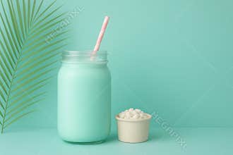 Refreshing mint green smoothie in a glass jar with a pink straw and a small dessert