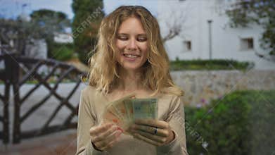 Woman displays banknotes while counting british pounds with a blonde young happy outdoor smile