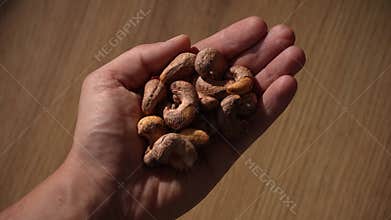 Hand holding raw cashew nuts above wooden table