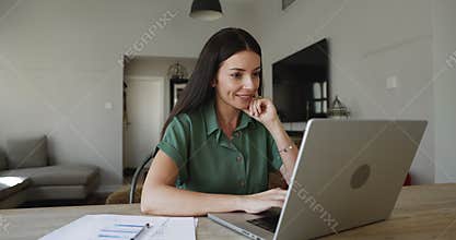 Smiling woman working from home, seated at table with laptop