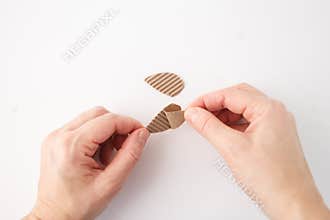 One hand holds the cardboard piece while the other is peeling it. The ridged texture is typical material for crafting or