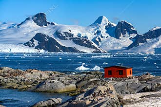 Petermann Island, beautiful Antarctic Island with penguins on rocks, abandoned station and snow covered mountains behind Ocean.