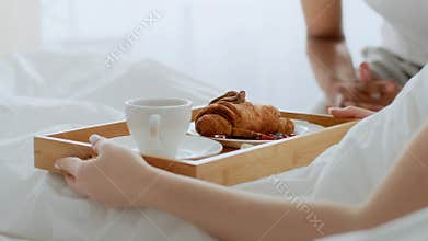 Couple enjoying breakfast in bed with coffee and croissants in their bedroom