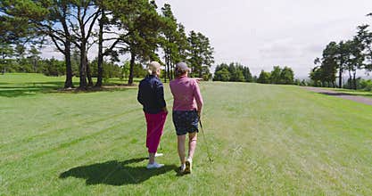 Female golf players standing with clubs and talking on golf course