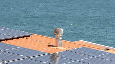 Metal chimney with a turbine ventilator is installed on a roof with solar panels near the sea