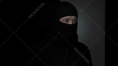 Individual in black balaclava looking sideways in shadow