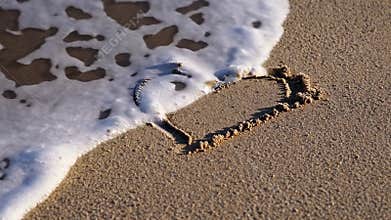 Heart drawn in smooth beach sand with ocean waves approaching shoreline