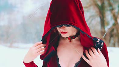 Fantasy mysterious woman queen hides face under hood cape cloak in winter forest