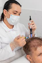 Trichologist doing man improve hair growth procedure, dermapen microneedling, vitamin injections