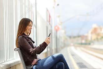 Happy woman texting on a smart phone in a train station